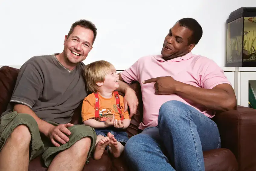 Two smiling men sitting with a young child on a sofa.